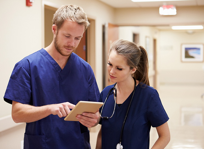 Medical Staff Looking At Digital Tablet In Hospital Corridor